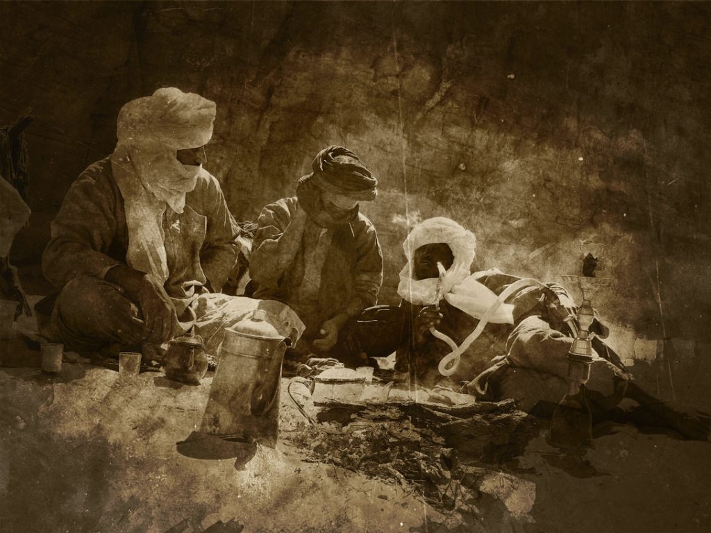 Alte Fotografie in Sepia-Farbe. Drei Männer mit Turban in einer Runde unterhalten sich und rauchen Wasserpfeife.